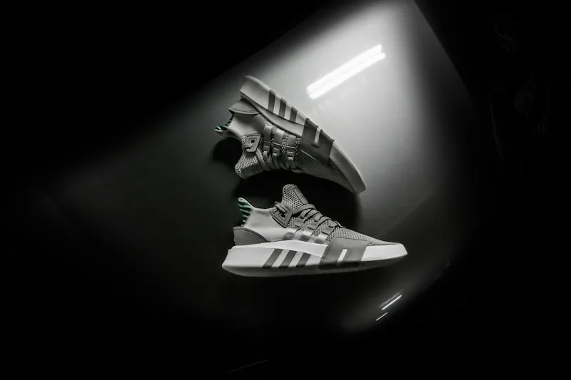 Two Adidas sneakers suspended in a dark studio.