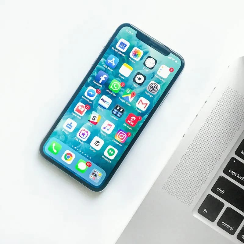 Apple iPhone on a white desk beside a laptop.
