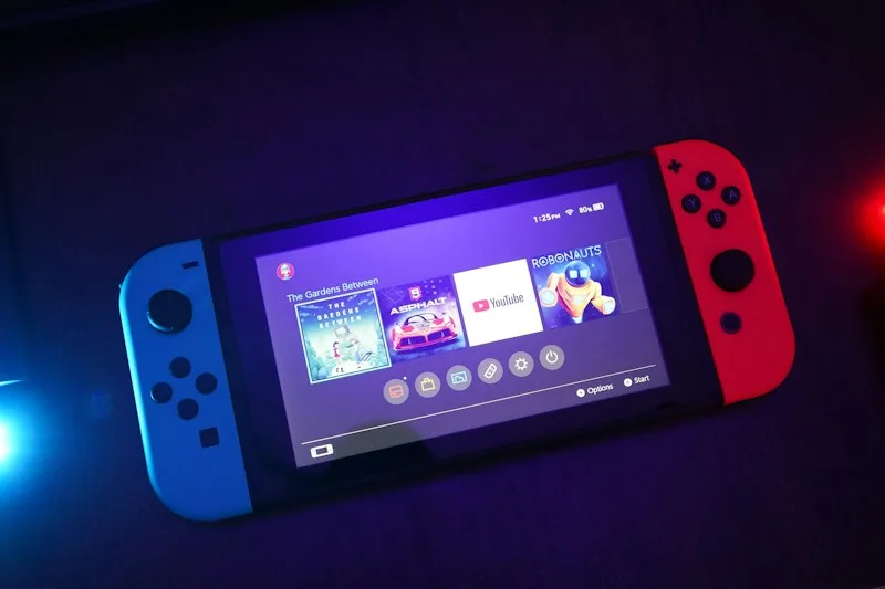 Nintendo Switch with blue and red controllers in colored light.