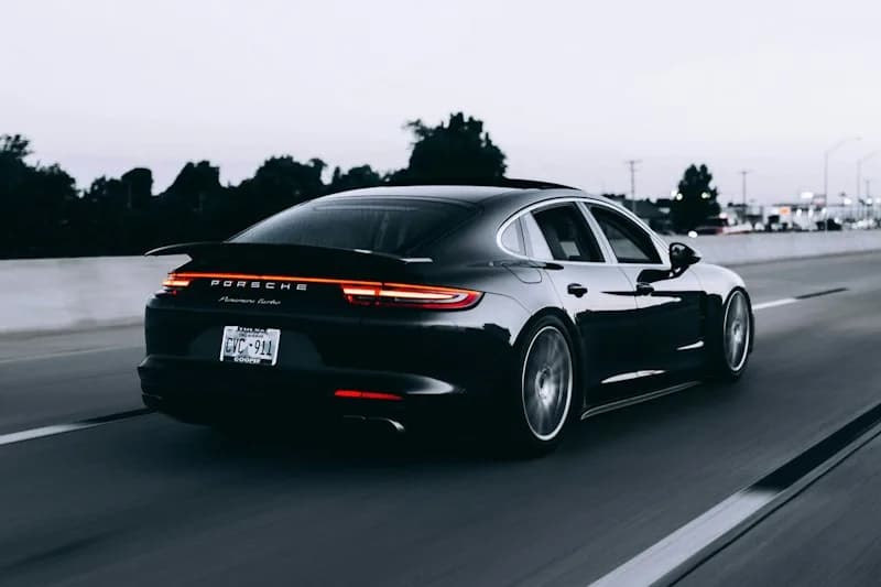 Dark Porsche photographed from behind on a road.