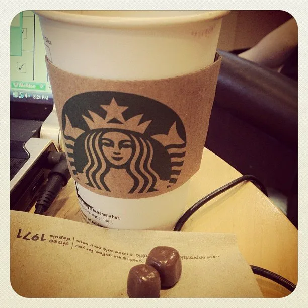 a cup of Starbucks coffee and tow tiny pieces of chocolates.